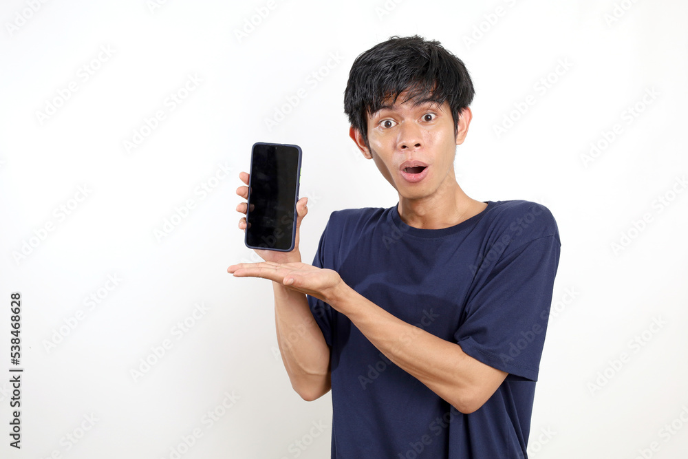 Happy amazed expression of asian young man standing while presenting blank cell phone screen. Isolated on white