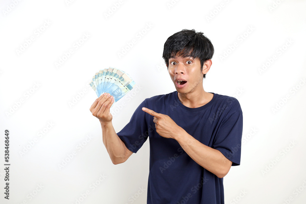 Surprised young asian man standing while holding Indonesian banknotes and pointing on it. Isolated on white Surprised young asian man standing while holding Indonesian banknotes and pointing on it. Isolated on white