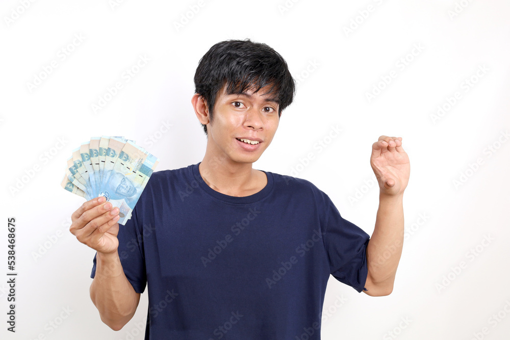 Happy young asian man standing while holding Indonesian banknotes and carrying something. Isolated on white Happy young asian man standing while holding Indonesian banknotes and carrying something. Isolated on white