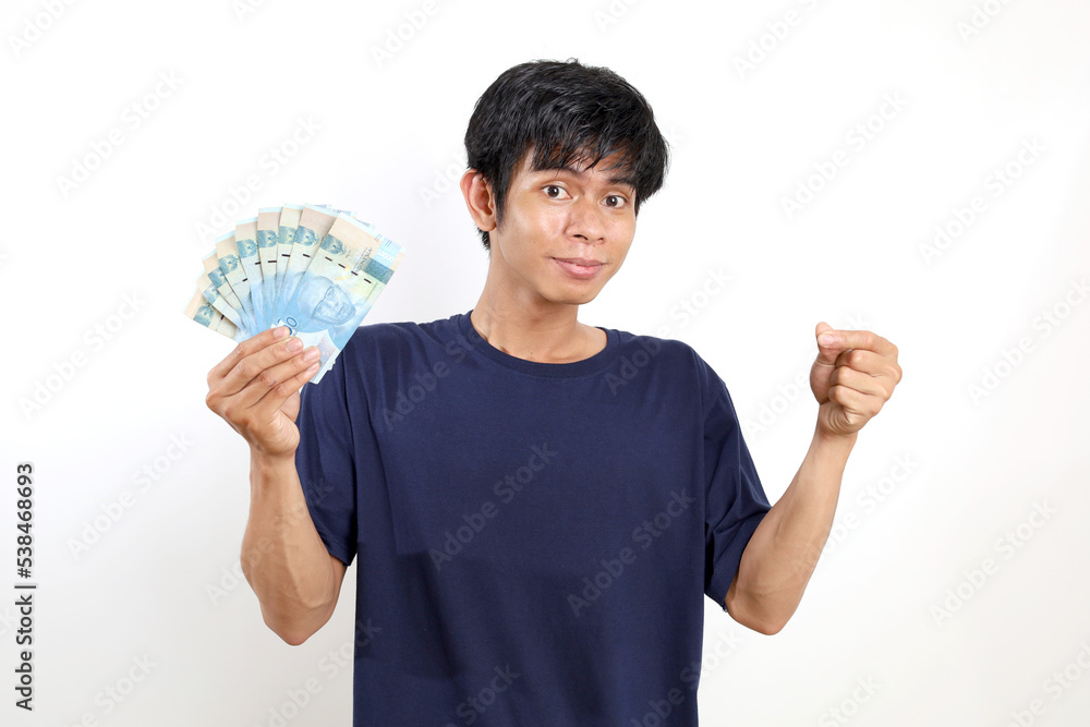 Happy young asian man standing while holding Indonesian banknotes and carrying something. Isolated on white Happy young asian man standing while holding Indonesian banknotes and carrying something. Isolated on white