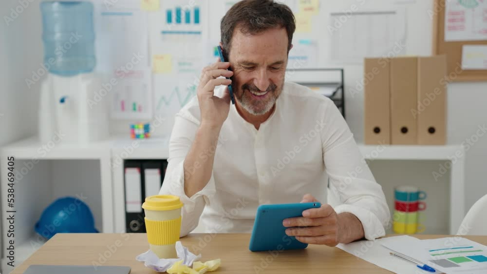Middle age man business worker talking on smartphone using touchpad at office Middle age man business worker talking on smartphone using touchpad at office