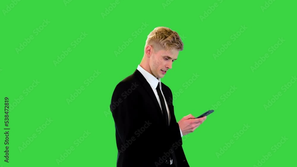 Attractive young businessman walks looking at the phone screen on a Green Screen, Chroma Key.