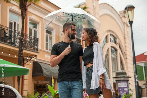 Young couple with umbrella enjoying time together under rain on city street