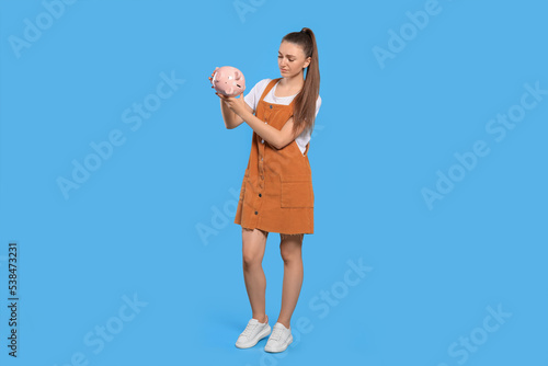Sad young woman with piggy bank on light blue background © New Africa