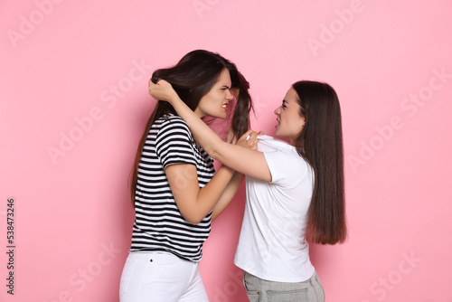 Aggressive young women fighting on pink background photo
