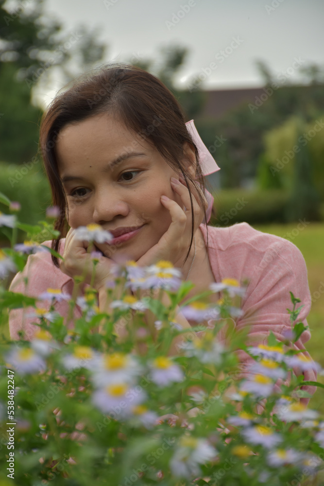 A woman sits and looks at real flowers in the middle of nature, looking like an outdoor flower garden. A woman sits and looks at real flowers in the middle of nature, looking like an outdoor flower garden.