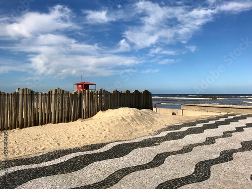 Coast of Tramandaí beach with a wooden fence close to the sea and a Copacabana style sidewalk over the sand. Southern Brazil.