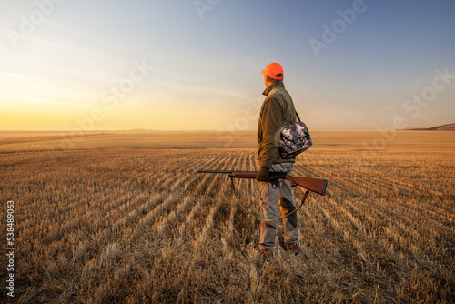 Hunter man with hunting gun to hunt in field at sunrise. Concept of autumn season, hunting banner with copy space.