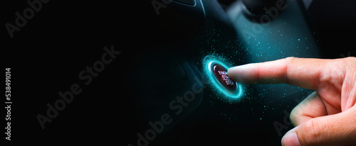 The driver palm as it presses the electric car engine start stop button with a blue light illuminated , panoramic banner with copy space on black background