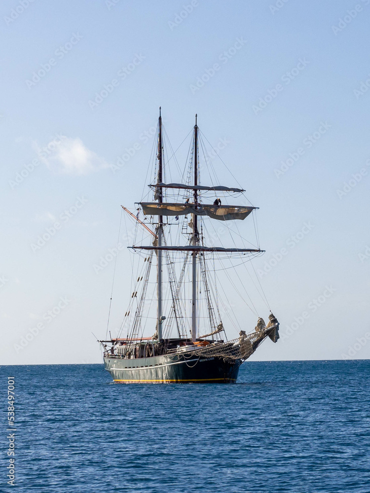 Tall ship at anchor on blue ocean against blue sky Tall ship at anchor on blue ocean against blue sky