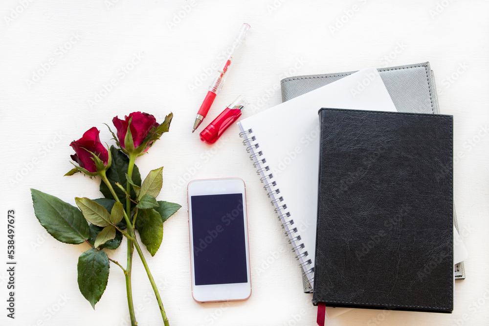 notebook planner, mobile for business work with rose flowers arrangement flat lay style on background white notebook planner, mobile for business work with rose flowers arrangement flat lay style on background white
