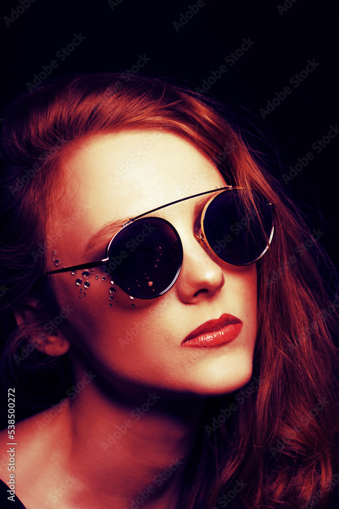Beautiful girl with round retro sunglasses and long hair close-up studio portrait. Model with glued jewelers around her eyes. Red color gradient map applied. Toned image with red and purple color Beautiful girl with round retro sunglasses and long hair close-up studio portrait. Model with glued jewelers around her eyes. Red color gradient map applied. Toned image with red and purple color
