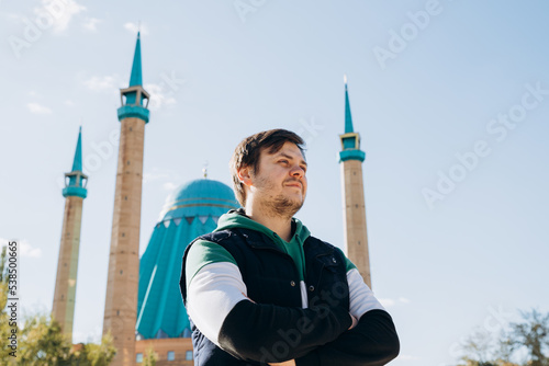 Looking away young man 34 years old against Muslim Mosque (Mashkhur Jusup Central Mosque) and autumn leaves trees. Russian migrant in Kazakhstan. Waist up lifestyle travel portrait, religion concept. photo