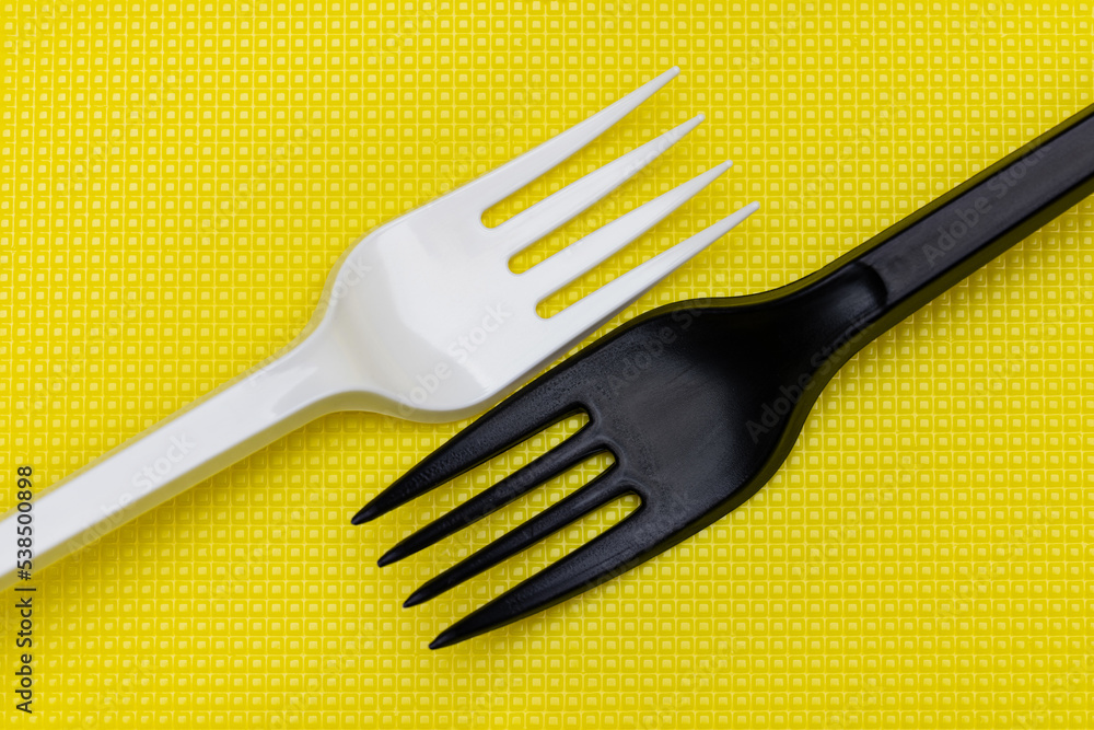 White and black plastic forks on a yellow background. White and black plastic forks on a yellow background.