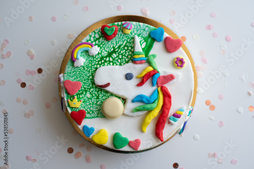 Cake decorate by handmade from color dough shape of unicorn and rainbow, colorful hearts on white-green background. Birthday party child decoration.