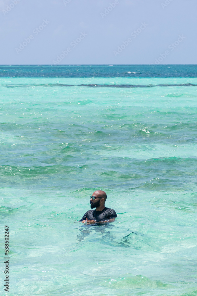 A picture of an Indian guy sitting in a swing in the shallow sea of Maldives and enjoying his vacation 