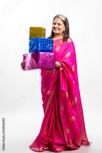 Indian older woman in traditional saree and holding gift box in hand