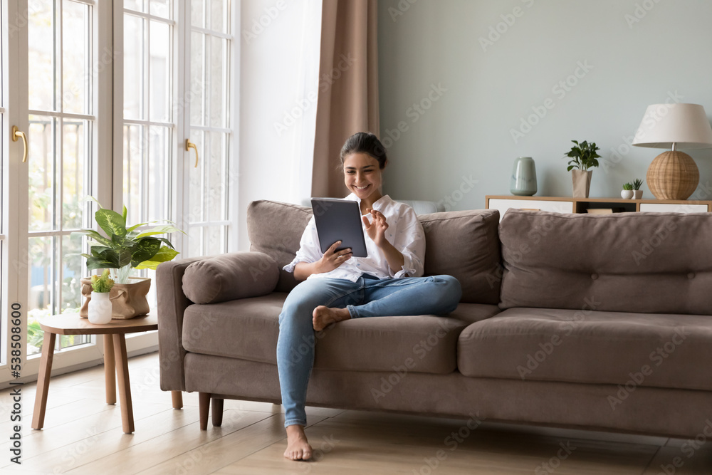Pretty Indian woman sit on sofa holds digital tablet, enjoy weekend leisure alone at home with electronic device using new application, buying goods on-line, make easy remote order. Modern tech usage Pretty Indian woman sit on sofa holds digital tablet, enjoy weekend leisure alone at home with electronic device using new application, buying goods on-line, make easy remote order. Modern tech usage