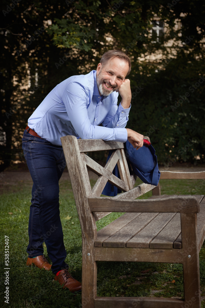 Fototapeta premium Man in blue suit with shirt and tie posing on bench in summer park