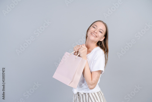 Seasonal sales and purchases. Portrait adorable happy female consumer walking and browsing free copy space, lady with pink package with new purchases isolated on gray Studio Wall, advertising