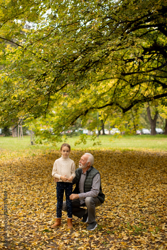 Grandfather spending time with his granddaughter in park on autumn day Grandfather spending time with his granddaughter in park on autumn day