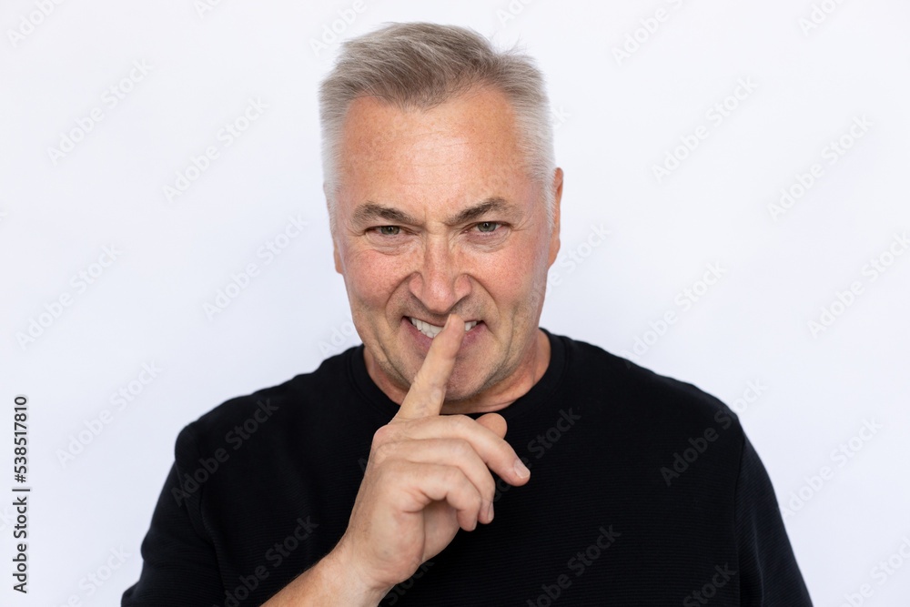 Portrait of angry senior man shushing. Displeased Caucasian male model in black T-shirt with gray hair looking at camera with finger on lips, asking to be quiet. Secret, silence concept. Portrait of angry senior man shushing. Displeased Caucasian male model in black T-shirt with gray hair looking at camera with finger on lips, asking to be quiet. Secret, silence concept.