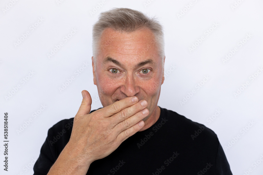 Closeup of happy Caucasian man covering mouth. Surprised elderly male model in black T-shirt with gray hair looking at camera, hiding smile or laugh. Surprise, good news concept. Closeup of happy Caucasian man covering mouth. Surprised elderly male model in black T-shirt with gray hair looking at camera, hiding smile or laugh. Surprise, good news concept.