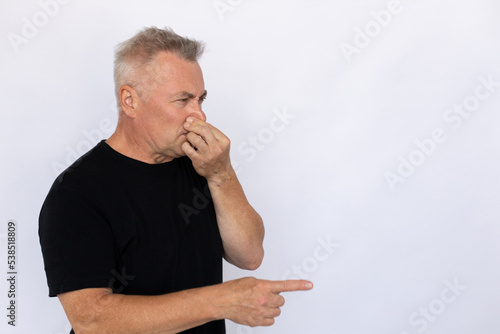 Senior man covering nose. Male model in black T-shirt pointing at empty space with covered nose, expressing disgust. Portrait, studio shot, disgust concept. photo