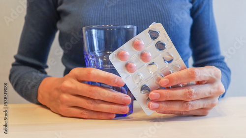 cold season, a girl in a blue sweater holds a glass of water and a pack of pills in her hands. Lack of vitamins in autumn and winter, uncontrolled medication, overdose, self-medication