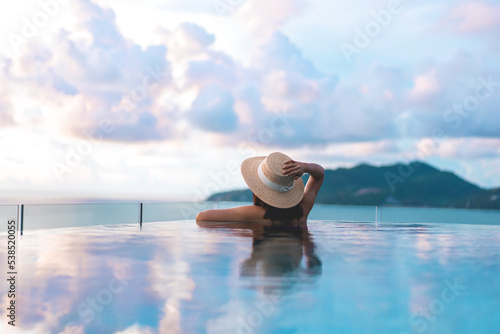 Rear view asia woman relax at outdoor luxury pool resort with sunset sky on holiday travel tropical photo