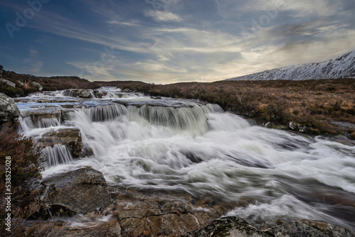 Epic Winter landscape image of River Etive in foreground with iconic snowcapped Stob Dearg Buachaille Etive Mor mountain in the background