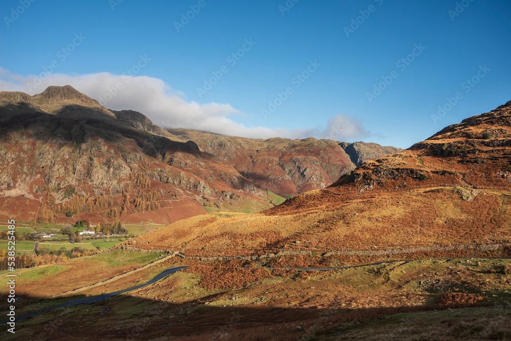 Colorful vibrant Autumn landscape image looking from Pike O'Blisco towards Langdale Pikes and Range with beautiful sungiht on mountains and valley