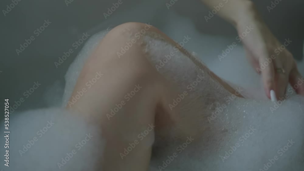 A beautiful shot of a young woman's legs in a bathtub filled with foam. The girl runs her hand over her leg with soap foam. High quality FullHD footage A beautiful shot of a young woman's legs in a bathtub filled with foam. The girl runs her hand over her leg with soap foam. High quality FullHD footage