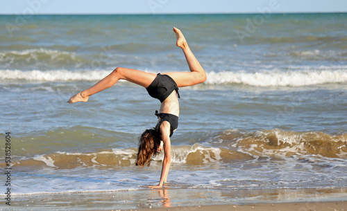 barefoot girl in black swimsuit from rhythmic gymnastics exercises on the seashore