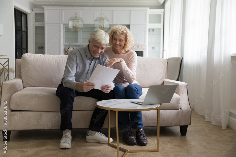 Attractive older couple reading received formal notification, smiling enjoy news, feel satisfied look happy, get mortgage approval, relish financial success, investment and profits, pension growth