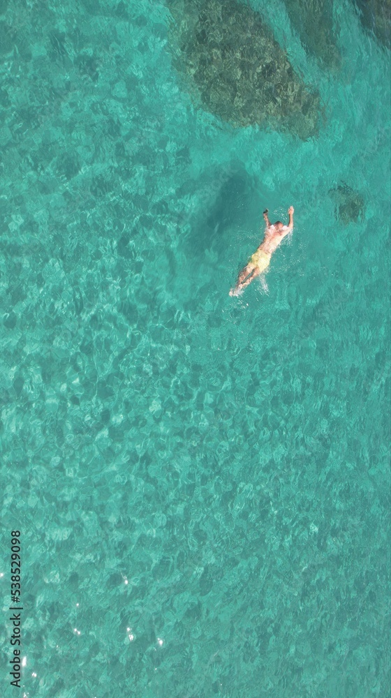 aerial view of joung man swiming on cristal clear waters on a beach of mallorca. Concept of holiday, summer, travel, tourism and relax	
