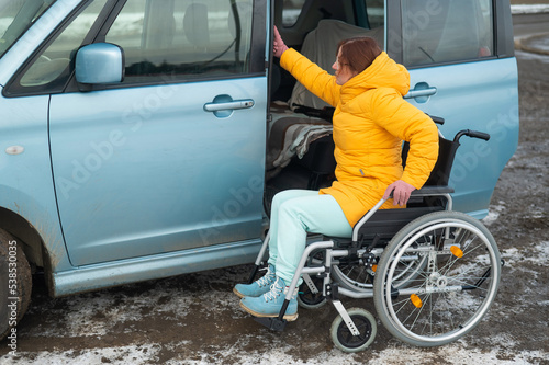 Caucasian woman in a wheelchair gets into the car. 
