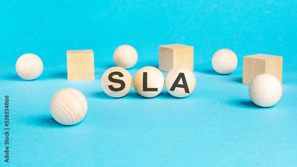 SLA word is made of wooden cubes lying on the blue table, business concept. SLA short for Service Level Agreement