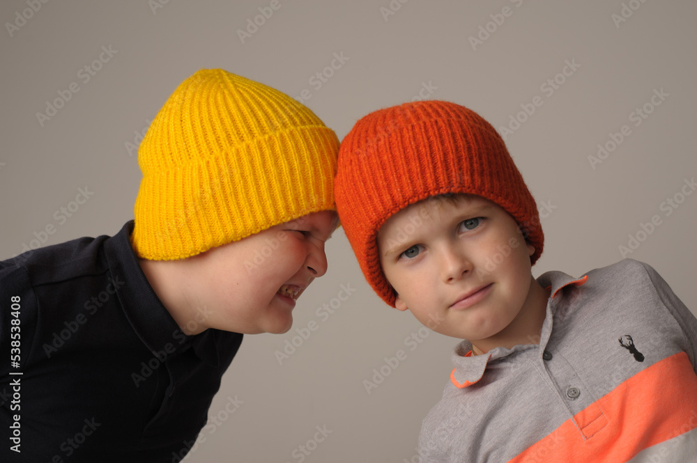 studio photo of two brothers aged 5 and 7 in bright knitted autumn hats on a gray background studio photo of two brothers aged 5 and 7 in bright knitted autumn hats on a gray background