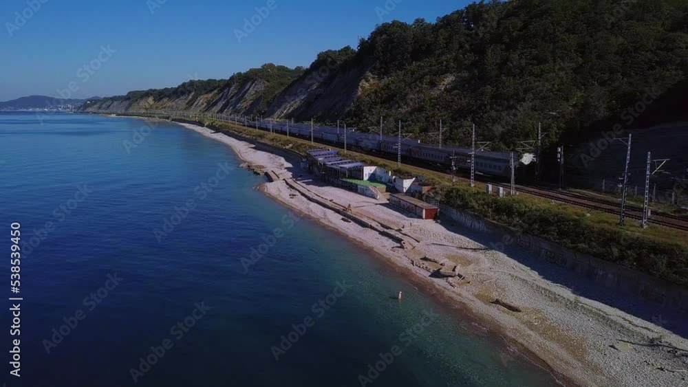 over the pebbly beaches near the railway with a standing passenger train along the Black Sea - aerial view on a sunny day over the pebbly beaches near the railway with a standing passenger train along the Black Sea - aerial view on a sunny day