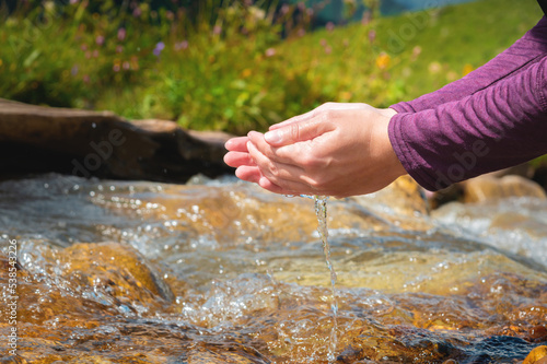 Close-up of water drops falling from female hands into a stream. The hand touches fresh water. A tourist drinks water from a reservoir in the mountains in summer on a sunny day