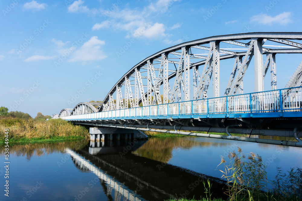 Metal bridge background. Road bridge construction. Empty asphalt road. Blue sky weather long bridge over Narew river. Tykocin village in Poland. Metal bridge background. Road bridge construction. Empty asphalt road. Blue sky weather long bridge over Narew river. Tykocin village in Poland.