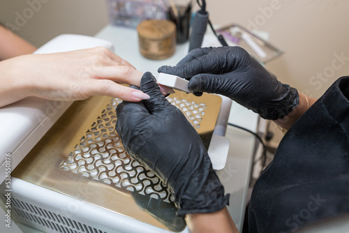 Manicurist makes a manicure to a client girl in a beauty salon.