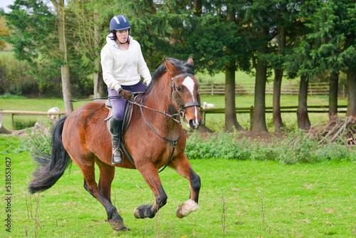 Pretty young rider and her beautiful horse enjoying cantering in field in Shropshire countryside on a summers day. 