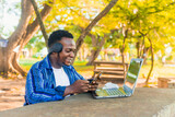 black African male student on headset smiling using card and mobile phone for shopping online