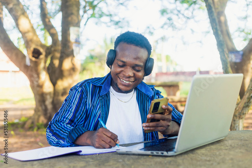 black Exciting African male student surfing the internet with a mobile phone to prepare school project