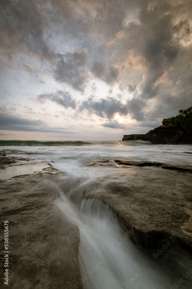 Obraz premium Sunset in tanah lot, bali with big rock cliff and coral reef using long exposure