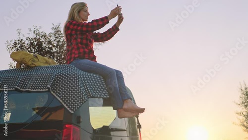 solo female traveler on car roof takes picture of sunset,spirit free alone girl sits on top of vehicle van enjoyng travel freedom photographing nature photo