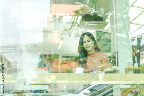A girl takes a phone call while having a cup of coffee with light reflection at the window. Lady sitting alone having a conversation through mobile phone beside a shop window with light reflection.