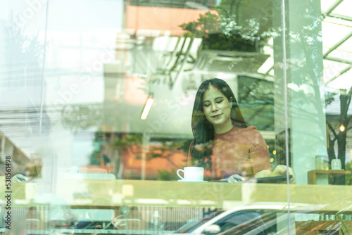A girl takes a phone call while having a cup of coffee with light reflection at the window. Lady sitting alone having a conversation through mobile phone beside a shop window with light reflection.